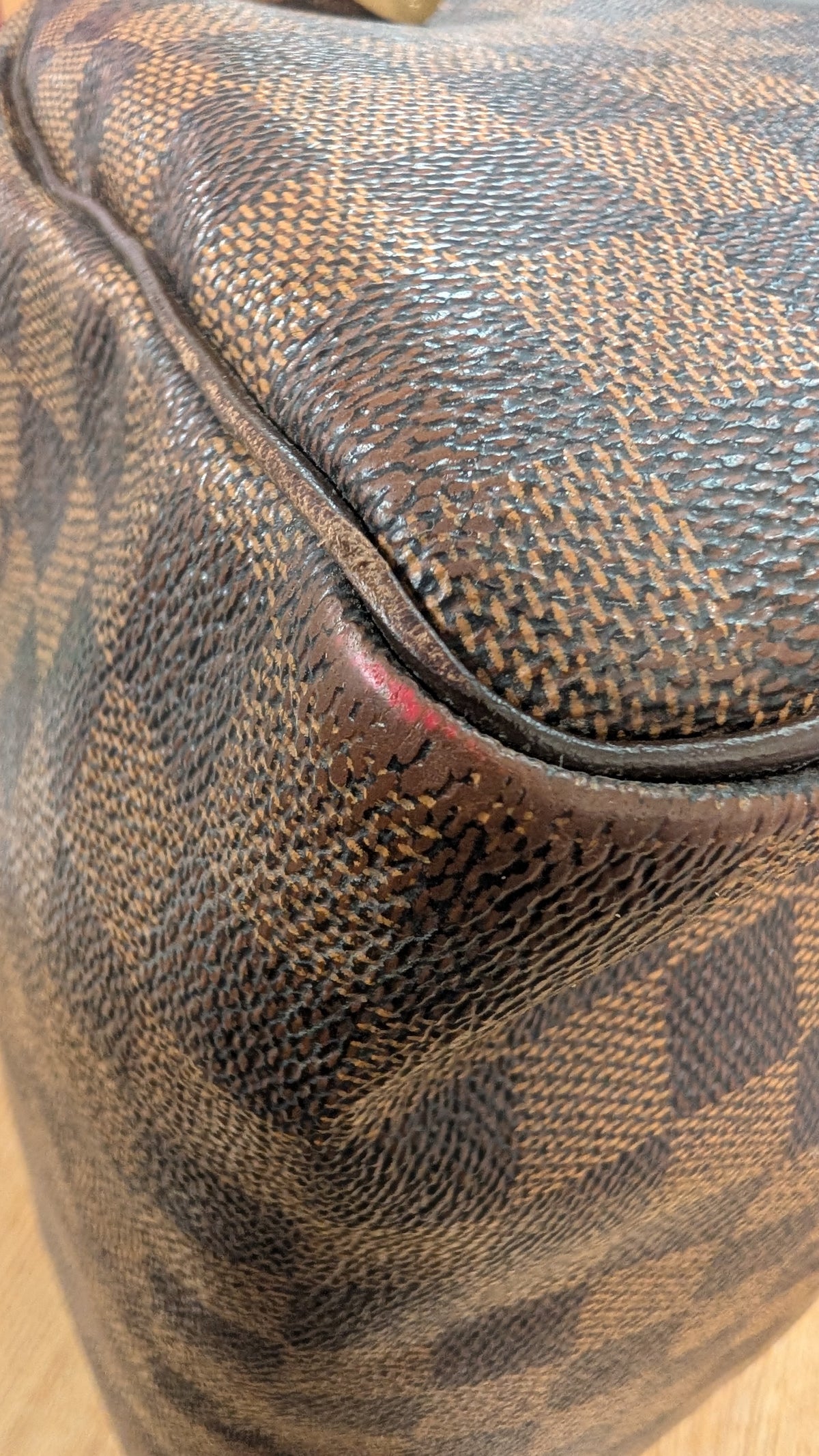 Close-up of a Louis Vuitton handbag in the classic Damier Ebene canvas, showing the textured brown and black checkered pattern and a small red scuff on the leather trim. Pre-Owned Louis Vuitton Speedy 25 Damier Ebene Coated Canvas Bag DU4151