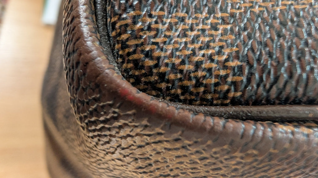 Close-up of a brown textured leather or faux-leather product corner with a woven houndstooth pattern in brown and beige visible on the upper section. Pre-Owned Louis Vuitton Speedy 25 Damier Ebene Coated Canvas Bag DU4151