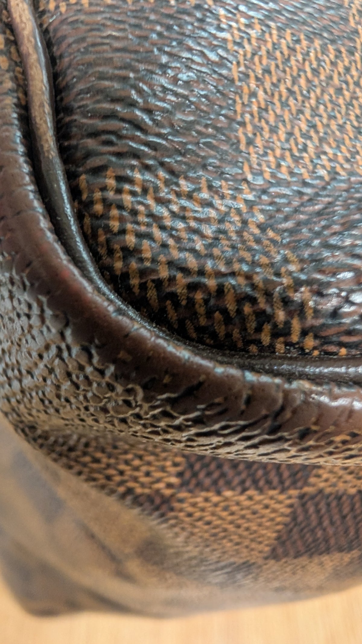 Close-up of a brown coated canvas or leather product with a dark brown checkerboard pattern and pebbled texture. Pre-Owned Louis Vuitton Speedy 25 Damier Ebene Coated Canvas Bag DU4151