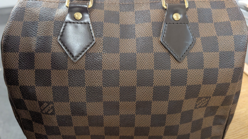 Close-up of a brown and dark brown checkerboard patterned handbag, featuring dark brown leather trim and gold-tone hardware. Pre-Owned Louis Vuitton Speedy 25 Damier Ebene Coated Canvas Bag DU4151