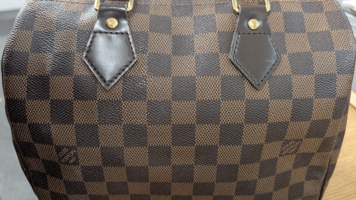 Close-up of a brown and dark brown checkerboard patterned handbag, featuring dark brown leather trim and gold-tone hardware. Pre-Owned Louis Vuitton Speedy 25 Damier Ebene Coated Canvas Bag DU4151