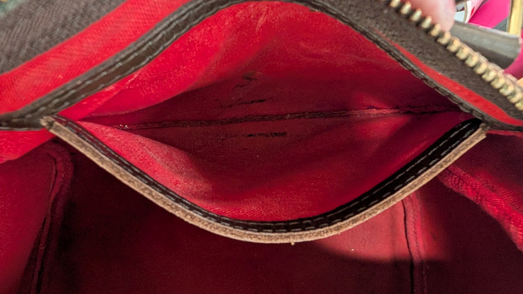 Close-up of the interior of a red handbag or wallet, showing a red fabric lining, dark brown stitched trim, and a gold zipper. Pre-Owned Louis Vuitton Speedy 25 Damier Ebene Coated Canvas Bag DU4151