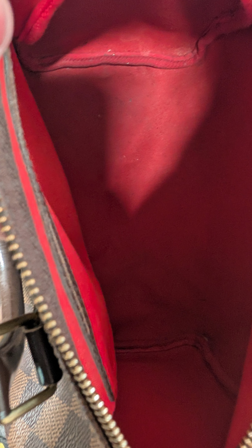 Close-up of the interior lining of a handbag, showing a bright red fabric interior with a gold-tone zipper and part of the brown monogram exterior. Pre-Owned Louis Vuitton Speedy 25 Damier Ebene Coated Canvas Bag DU4151