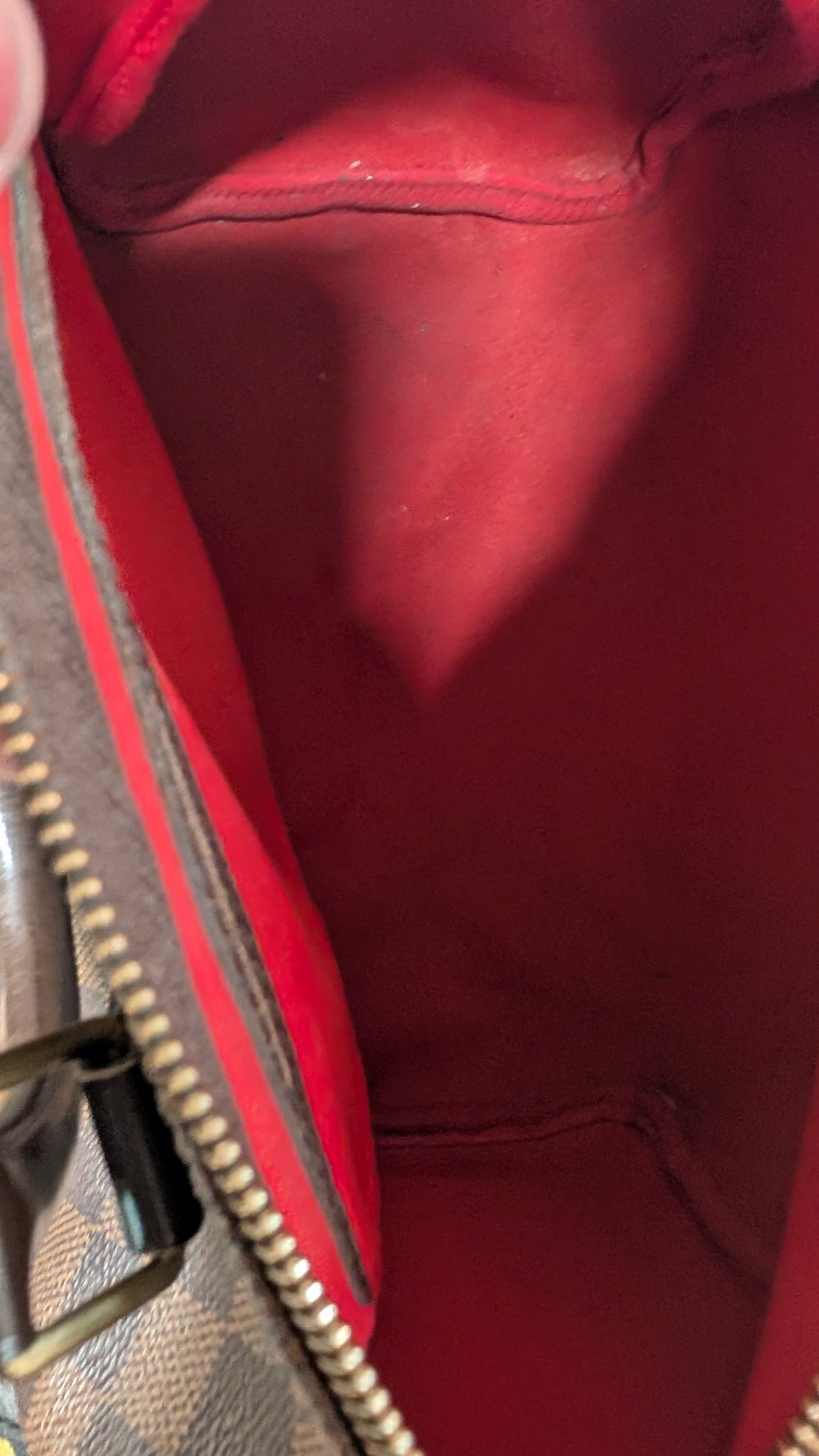 Close-up of the interior lining of a handbag, showing a bright red fabric interior with a gold-tone zipper and part of the brown monogram exterior. Pre-Owned Louis Vuitton Speedy 25 Damier Ebene Coated Canvas Bag DU4151