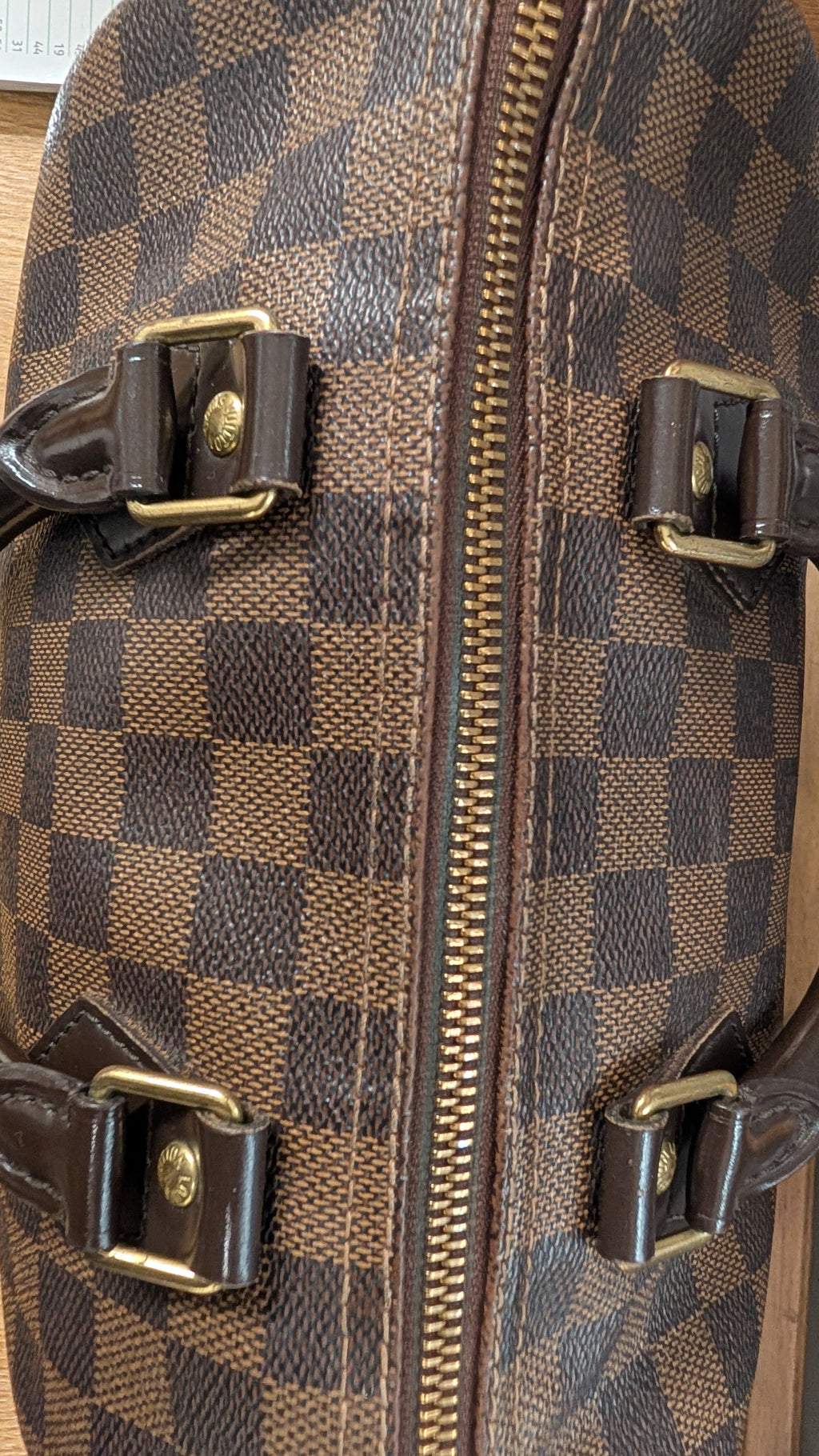 Close-up of a brown and dark brown checkerboard patterned bag with gold-tone hardware and a central zipper. Pre-Owned Louis Vuitton Speedy 25 Damier Ebene Coated Canvas Bag DU4151