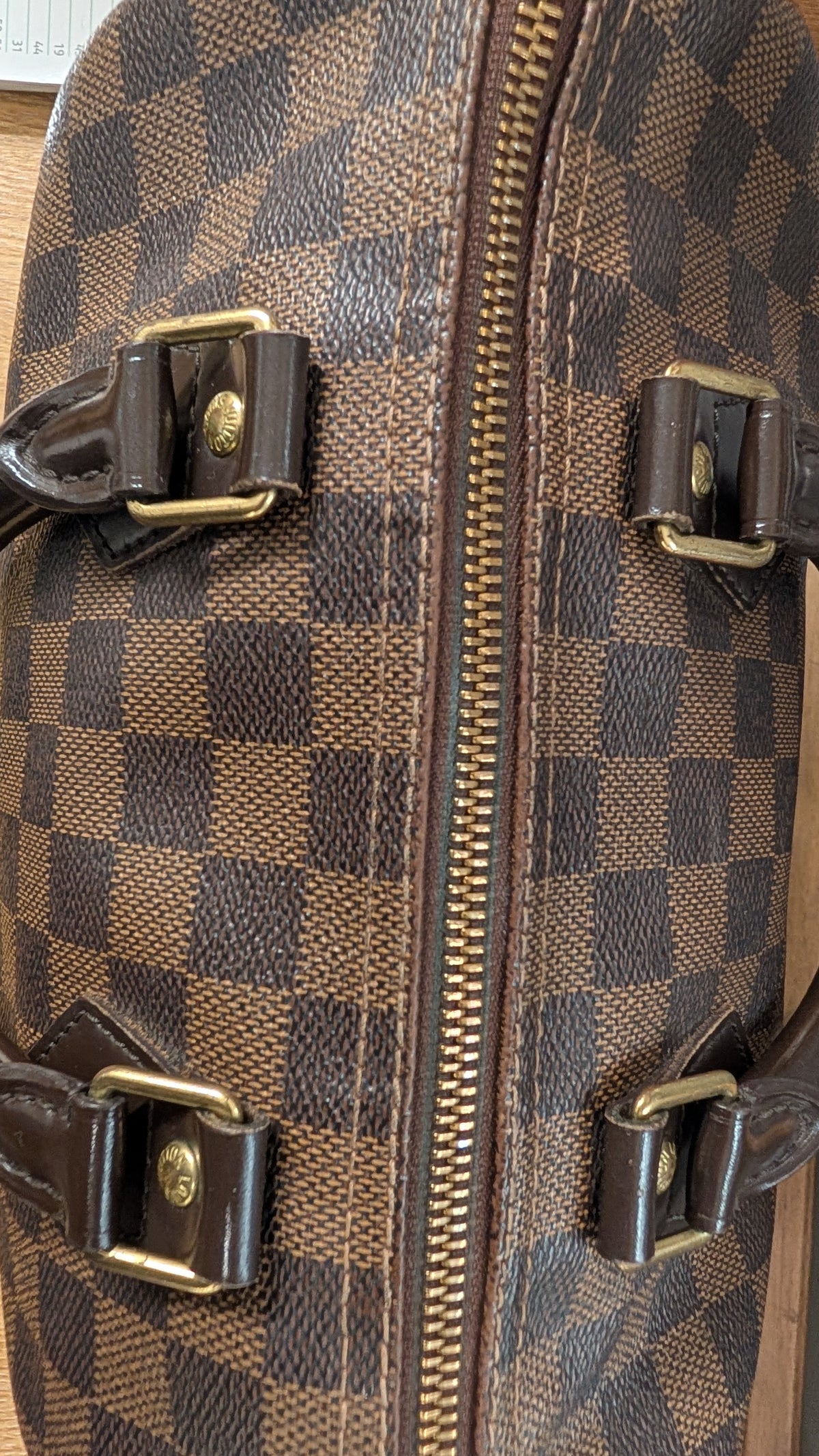 Close-up of a brown and dark brown checkerboard patterned bag with gold-tone hardware and a central zipper. Pre-Owned Louis Vuitton Speedy 25 Damier Ebene Coated Canvas Bag DU4151