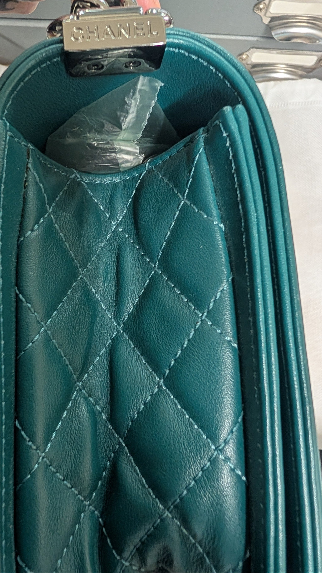 Close-up of a teal quilted leather handbag with a silver-tone metal clasp engraved with 'CHANEL'. Pre-Owned Chanel Boy Hang Bag – Teal Quilted Leather with Ruthenium-Tone Hardware