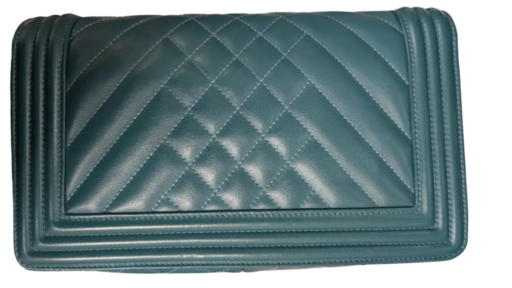 A teal green quilted leather shoulder bag with a diamond pattern, featuring a silver chain strap on the left side, photographed on a light-colored fabric surface. Pre-Owned Chanel Boy Hang Bag – Teal Quilted Leather with Ruthenium-Tone Hardware