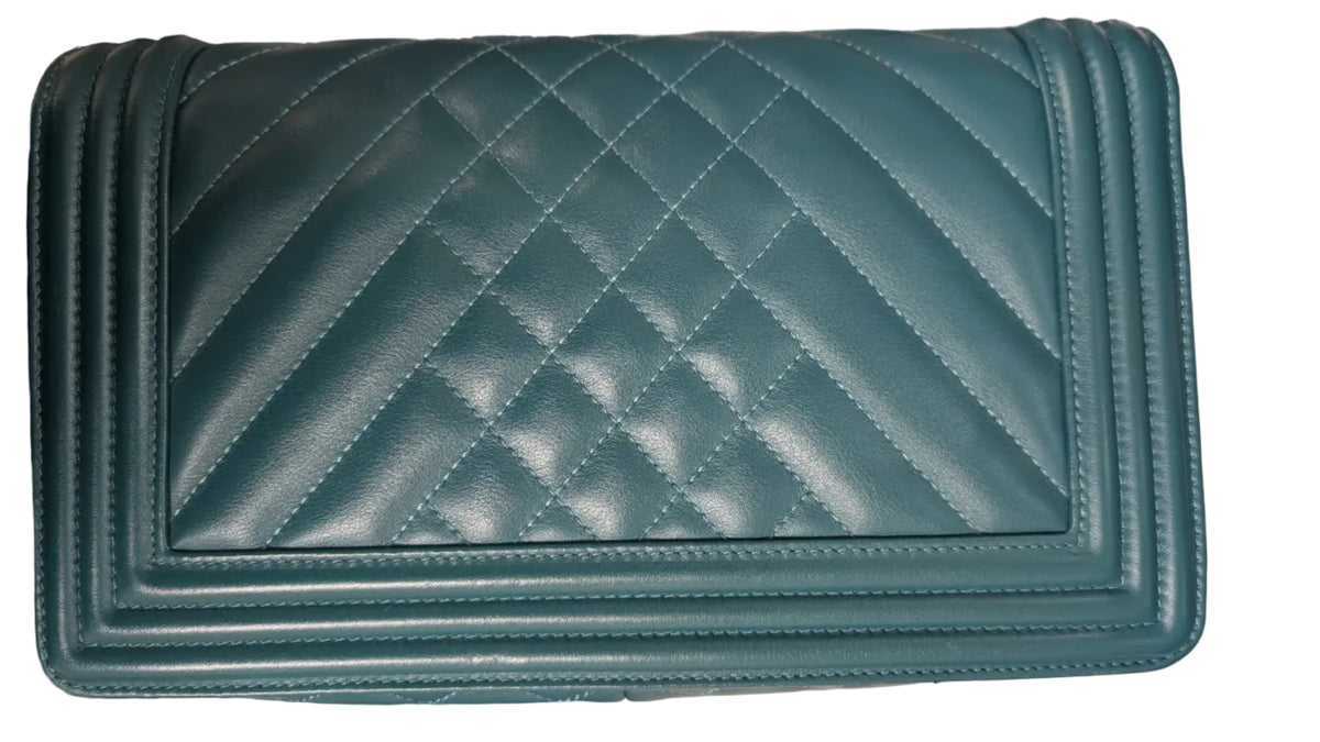 A teal green quilted leather shoulder bag with a diamond pattern, featuring a silver chain strap on the left side, photographed on a light-colored fabric surface. Pre-Owned Chanel Boy Hang Bag – Teal Quilted Leather with Ruthenium-Tone Hardware