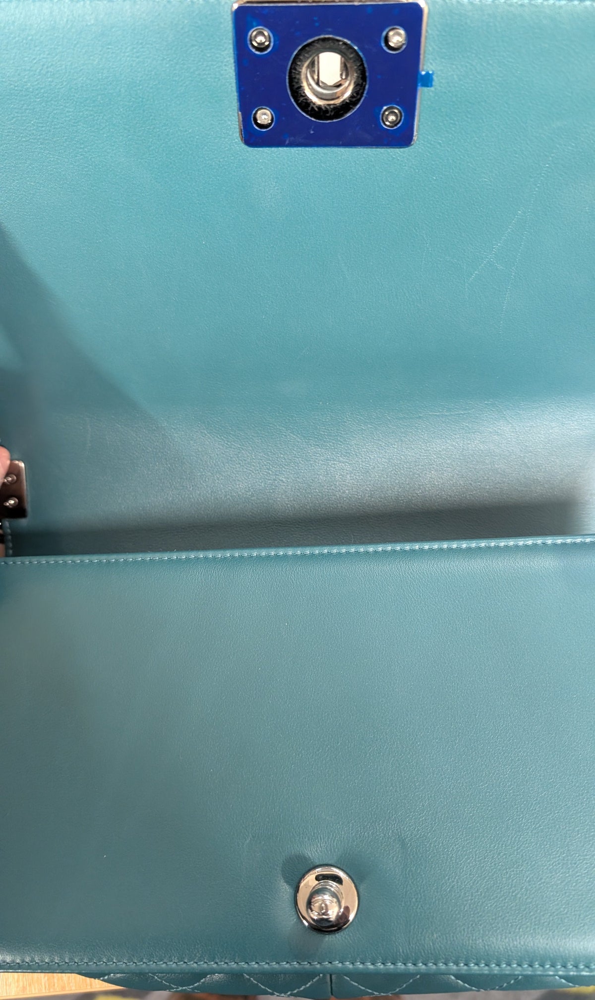 Close-up of a turquoise blue leather clutch or handbag interior showing a snap button closure and a blue metal accent  Pre-Owned Chanel Boy Hang Bag – Teal Quilted Leather with Ruthenium-Tone Hardwareplate.