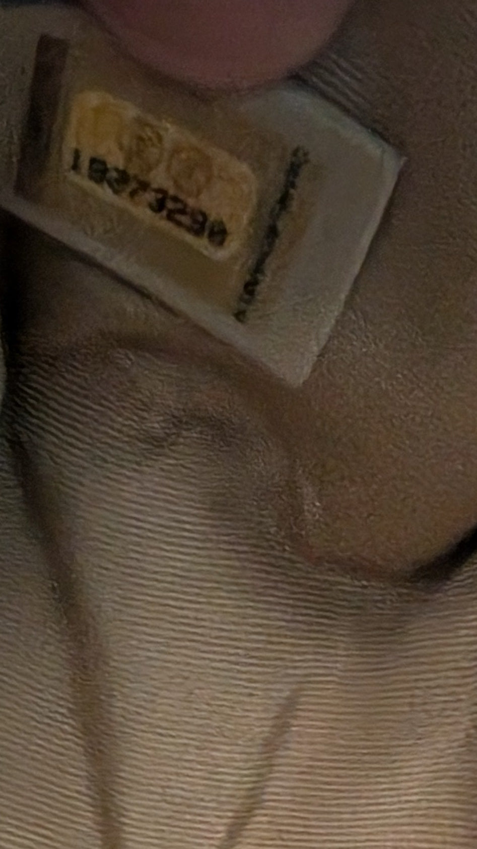 A close-up of a beige ribbed fabric item, likely a cushion or pillow, with a small sewn label visible on the side. Pre-Owned Chanel Boy Hang Bag – Teal Quilted Leather with Ruthenium-Tone Hardware 