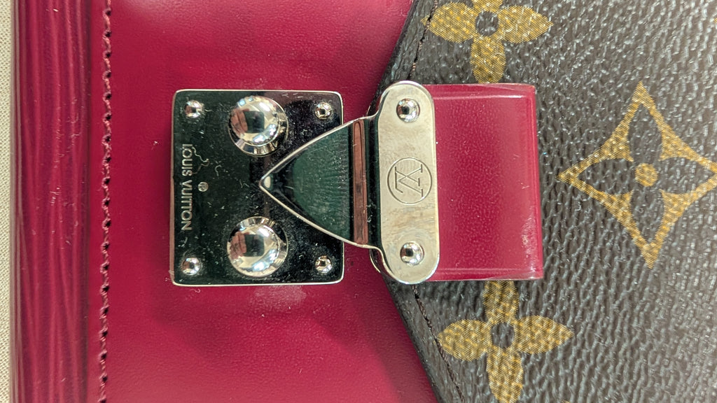 Close-up of a Louis Vuitton bag showing a magenta leather strap attached to a brown monogram canvas section with a silver-tone metal clasp. Pre-Owned Louis Vuitton Portefeuille Marie-Rose Clutch Wallet – Fuchsia Epi Leather & Monogram Canvas