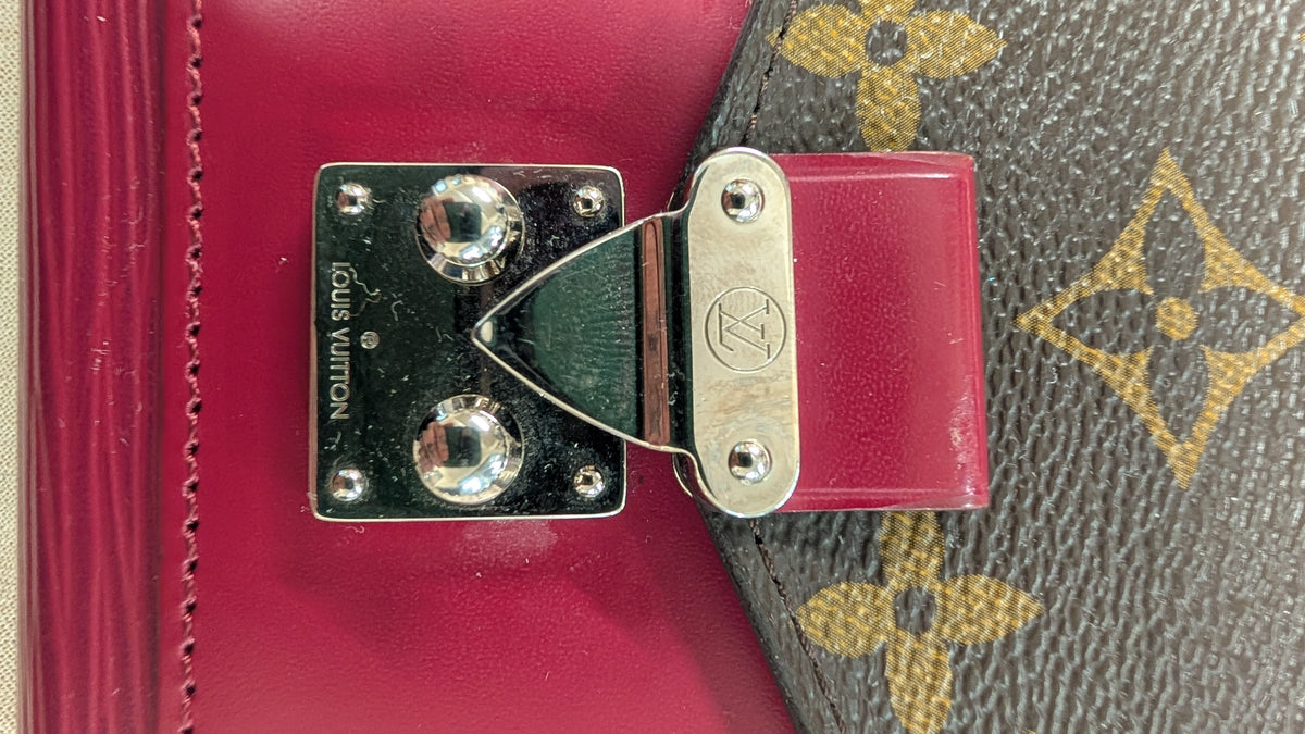 Close-up of a Louis Vuitton bag showing a magenta leather strap attached to a brown monogram canvas section with a silver-tone metal clasp. Pre-Owned Louis Vuitton Portefeuille Marie-Rose Clutch Wallet – Fuchsia Epi Leather & Monogram Canvas