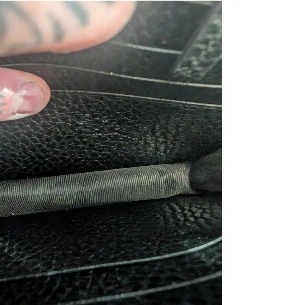Close-up of a black textured leather or faux-leather item with a stitched seam and a gray ribbed fabric strip running horizontally. Pre-Owned Gucci Interlocking G Wallet on Chain – Black Leather