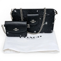 A Coach crossbody bag in black textured leather with silver chain straps and white star print, shown alongside a matching small flap wallet and a white Coach dust bag on a white background. Pre-Owned Coach Black Celestial Print Crossbody Pouch Set – Excellent Condition
