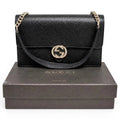A black pebbled leather Gucci shoulder bag with a gold-tone interlocking GG logo and chain strap, displayed on top of a dark brown Gucci shoebox against a white background. Pre-Owned Gucci Interlocking G Wallet on Chain – Black Leather